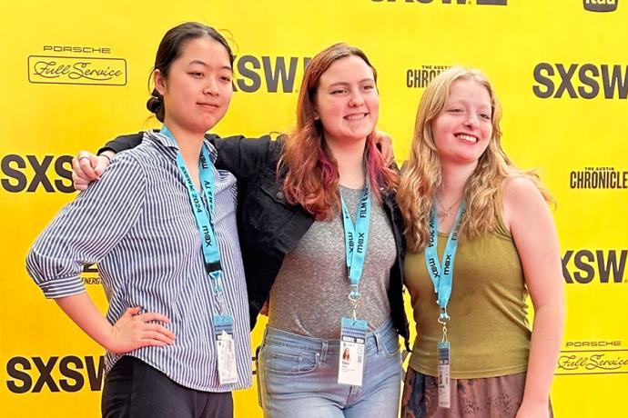 Three Film & New Media students pose in front of a yellow step-and-repeat.