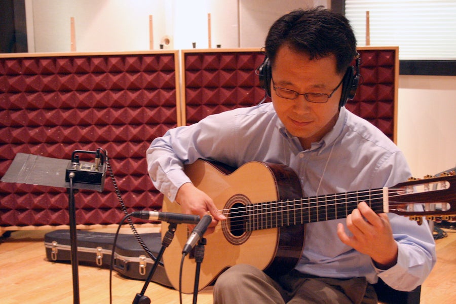 A man plays guitar in a recording studio.