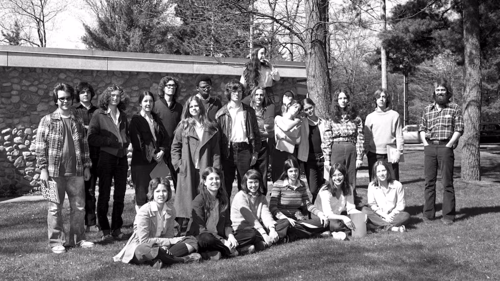 A group of young adults and one older adult posing outside in a park-like setting.