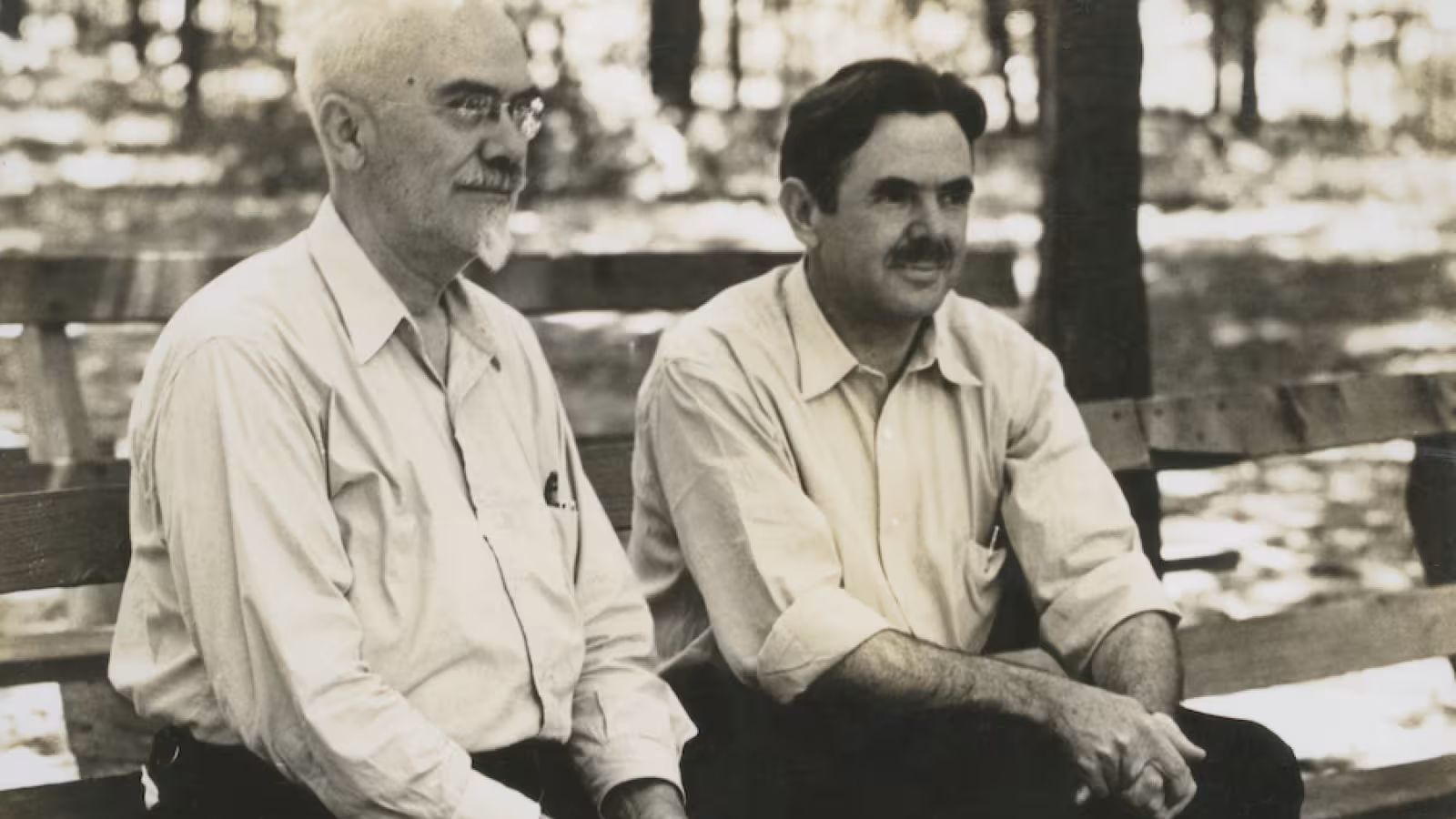  Black and white photo of T.P. Giddings and Joseph Maddy  sitting on a bench in a wooded area.