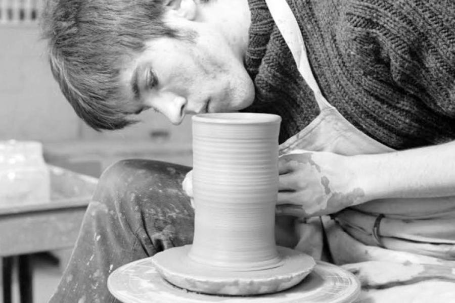 A young man crafts a vessel on a pottery wheel