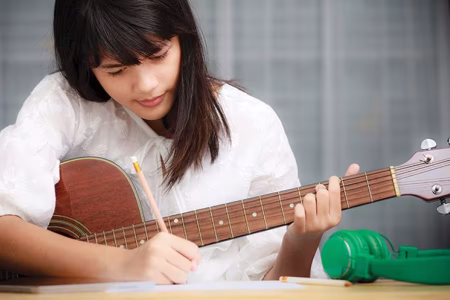 A girl jots down notes while playing guitar