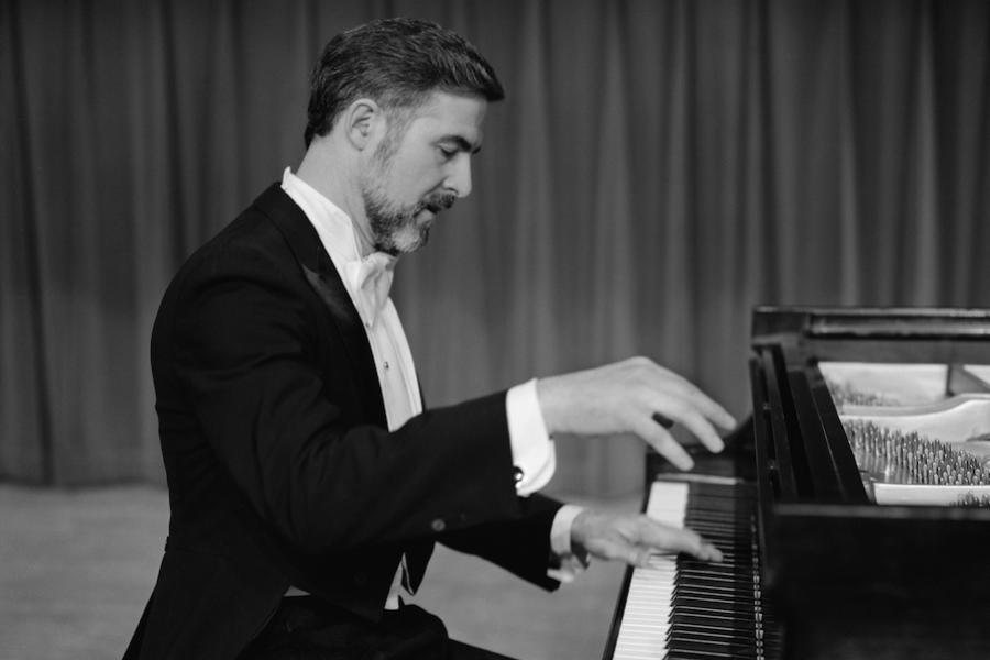 A male in his 50s, dressed in white tie and tails, performs at the piano. 