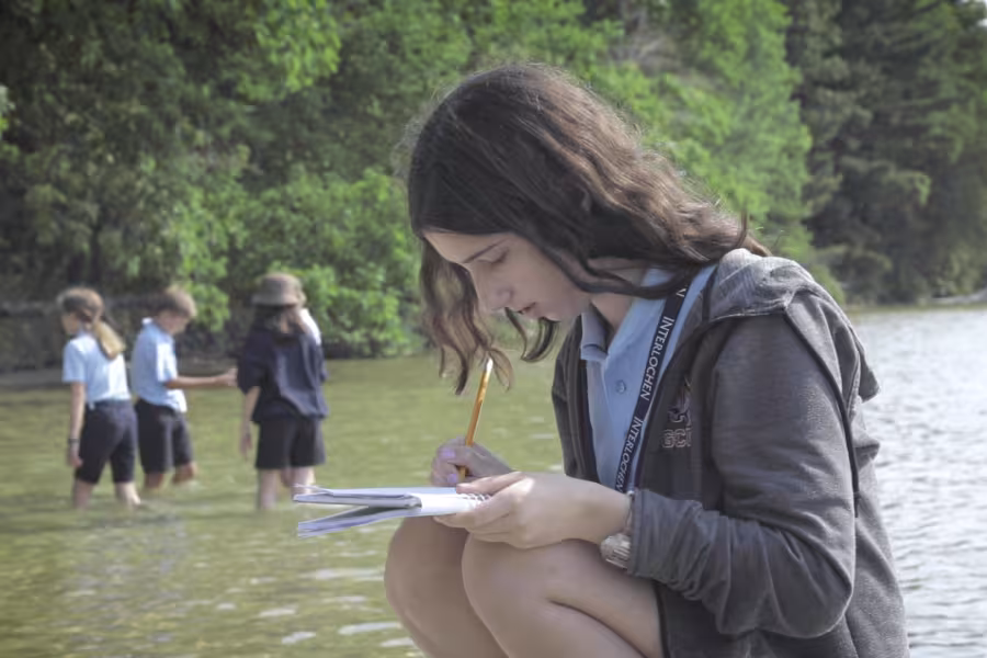 A girl writes next to a lake