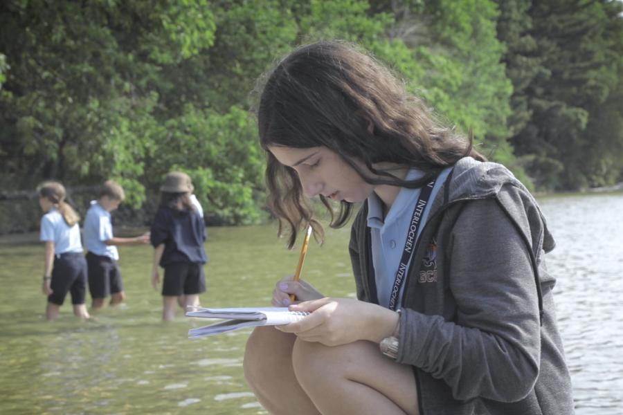 A girl writes next to a lake