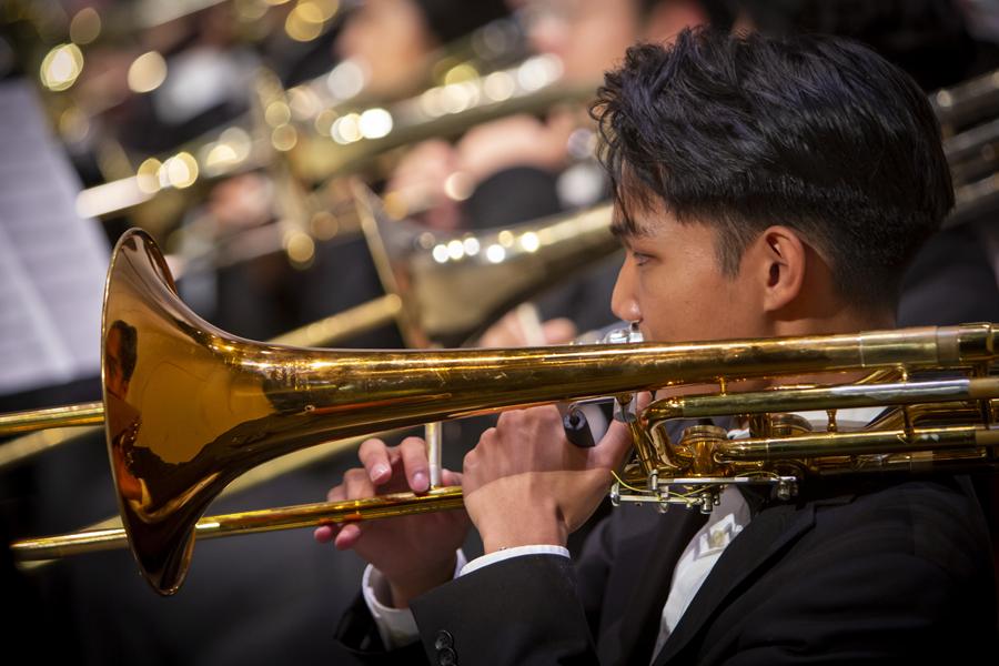 A male academy student playing a trombone in a formal concert