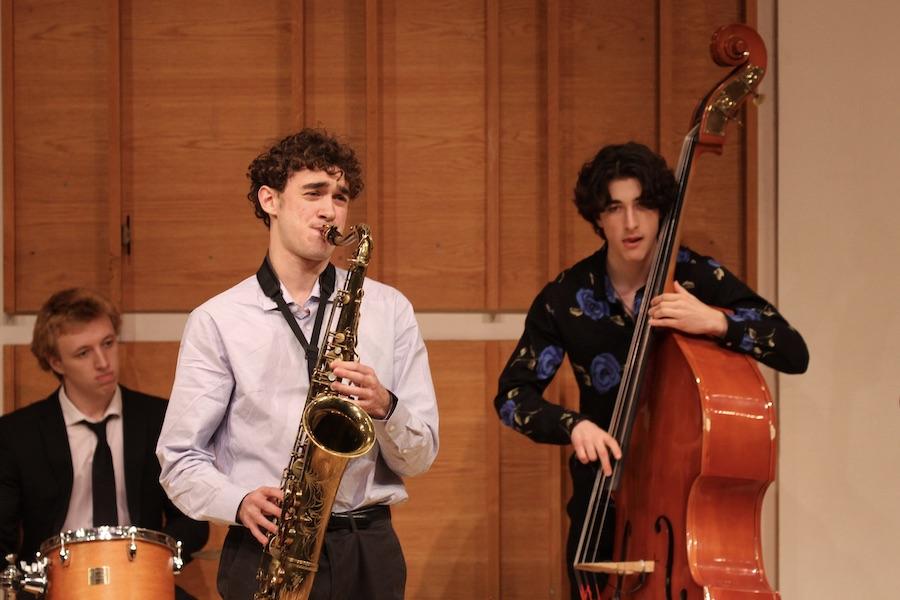 A student in a white shirt with a passionate expression plays saxophone. He is surrounded by members of his jazz band.