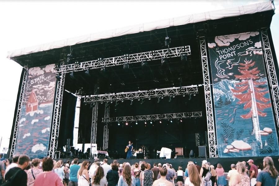 A singer stands in the center of a stage in front of a large crowd.