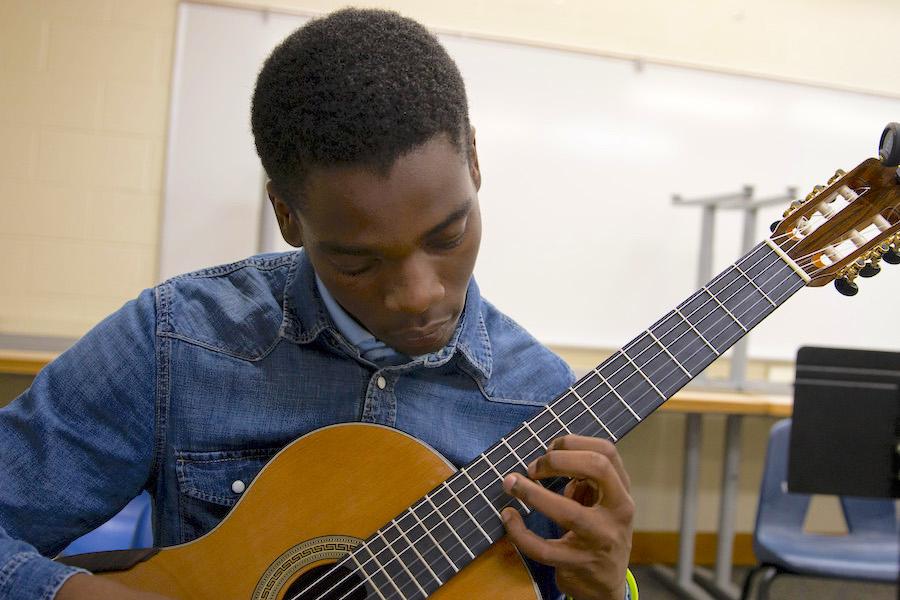 A man plays acoustic guitar in a classroom