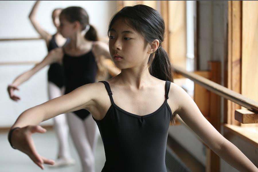 A girl ballerina practicing her posture at the barre. 