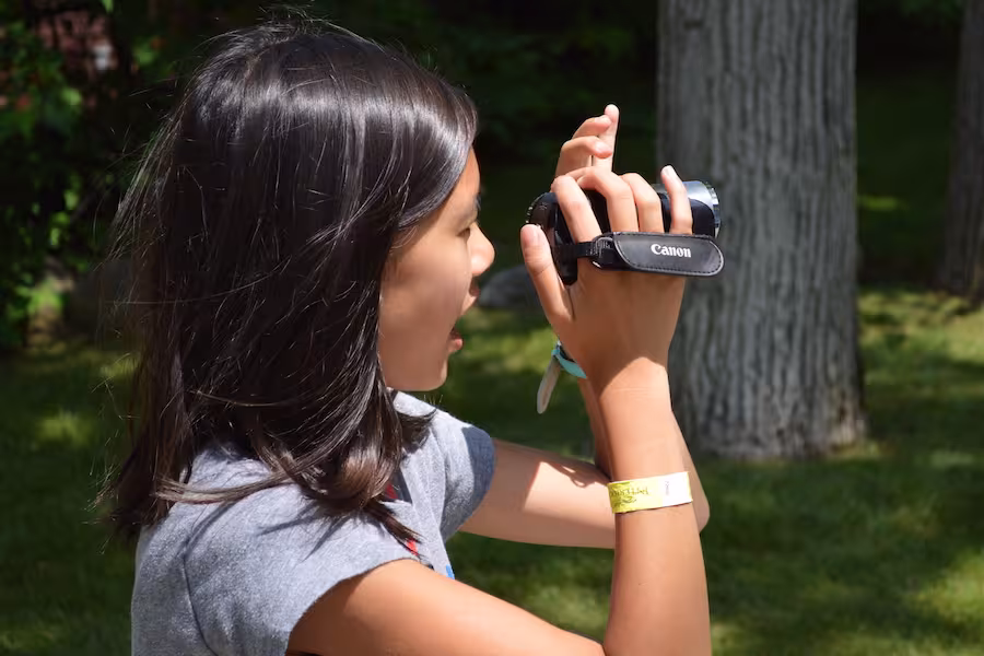A girl looking through a video camera outside. 