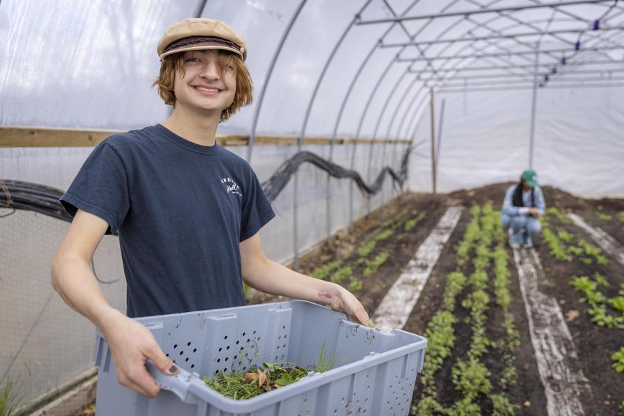 A student working in a hoop house garden smiles at the camera.