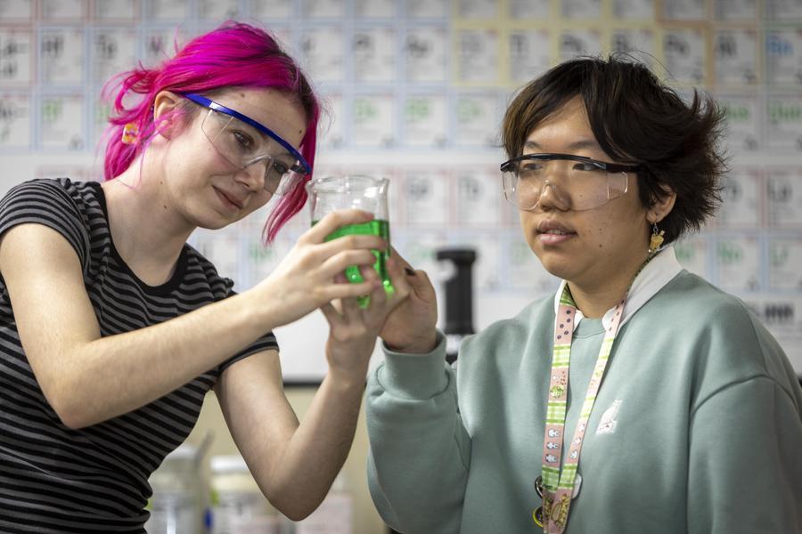 2 students in chemistry class looking at green liquid in a beaker 