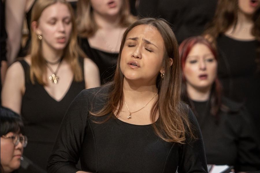 A soloist in a black dress sings in front of a choir.