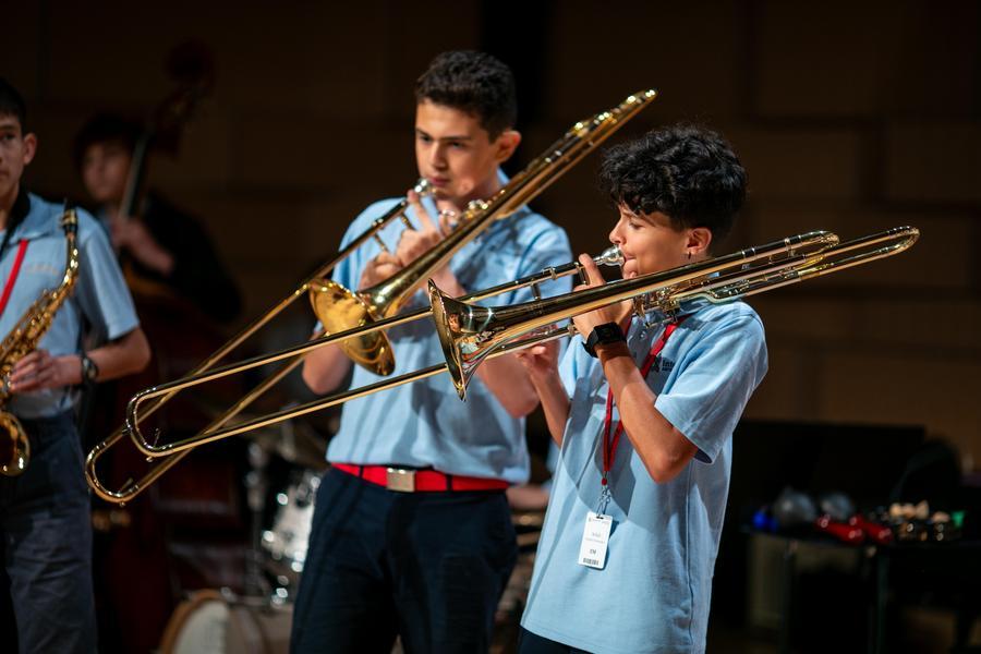 Two students in uniform play trombones.