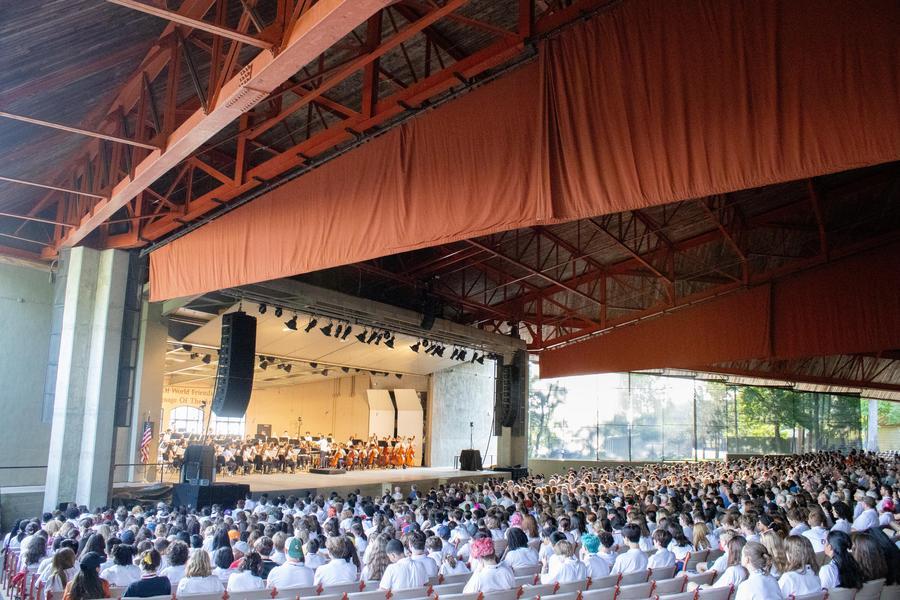 A student orchestra performs onstage in front of a large audience.