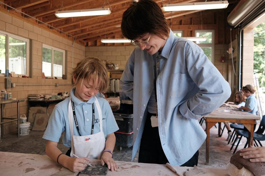 A young student works on a ceramics project under the supervision of an instructor.