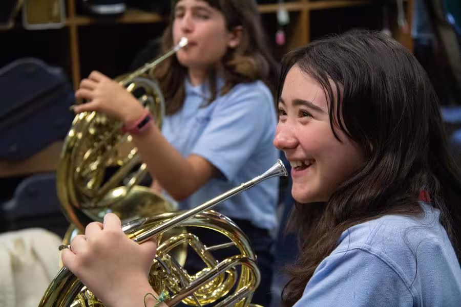A smiling camp student holding a french horn