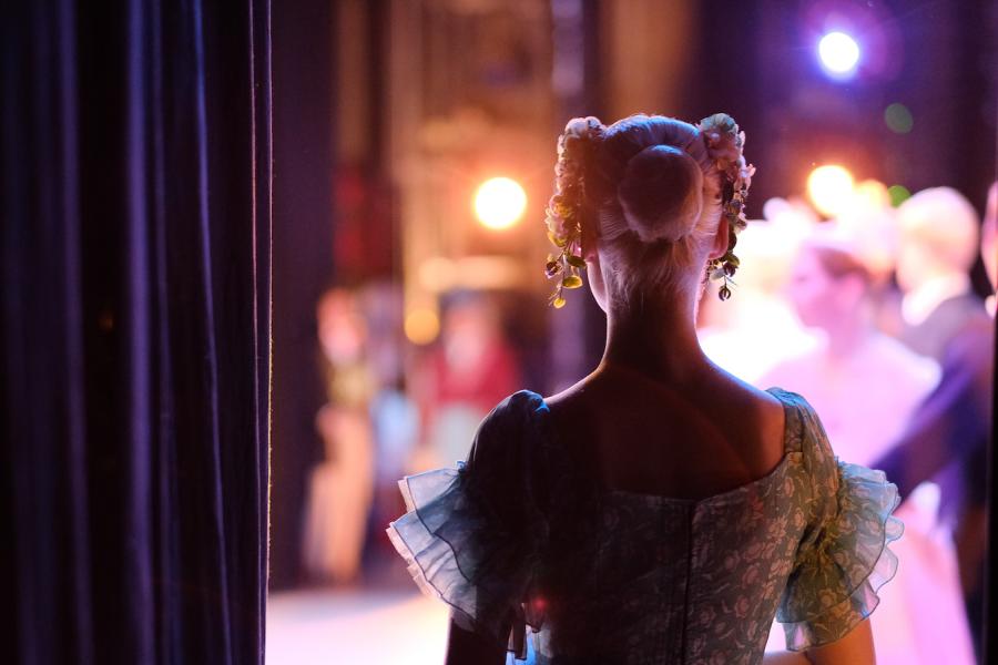 A woman is offstage and behind the curtain looking out to performers on stage.