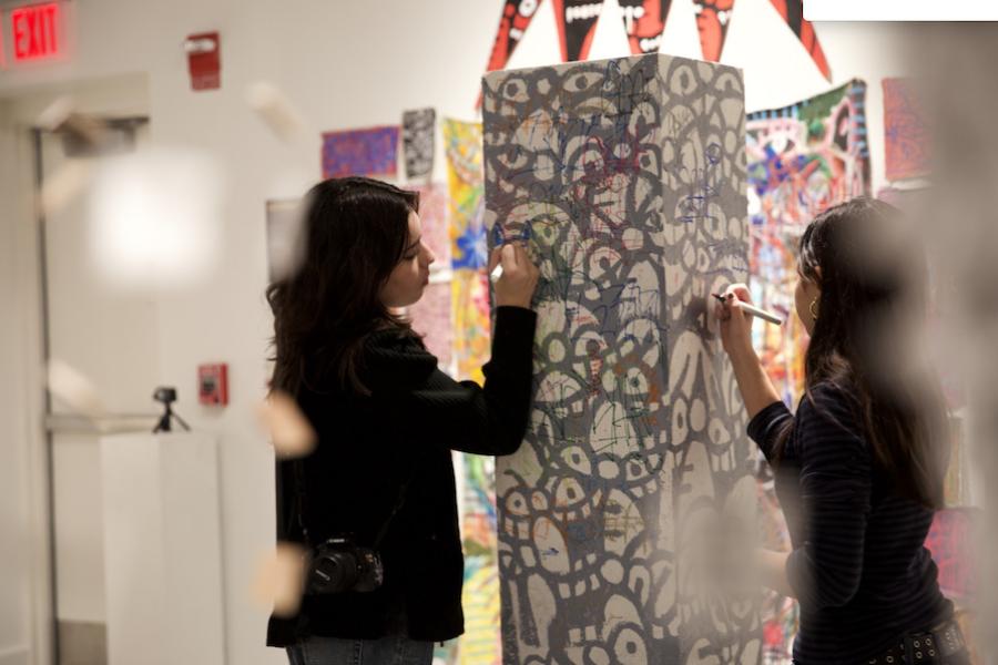 Two students draw with markers on a patterned pillar.