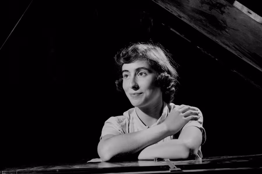 A camp student sits at the piano and crosses her arms. 