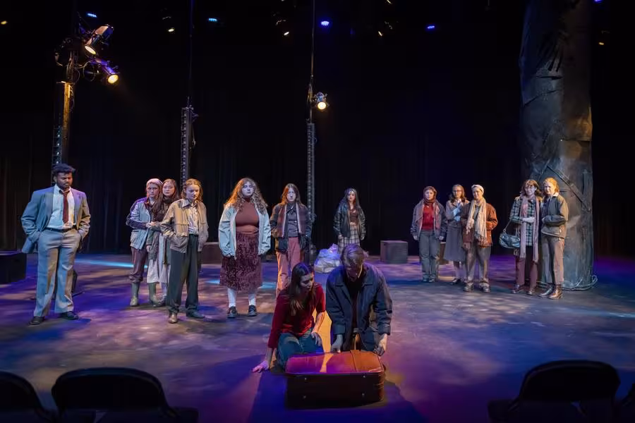 A group of students stand on stage beside a large metal tree-shaped set piece.