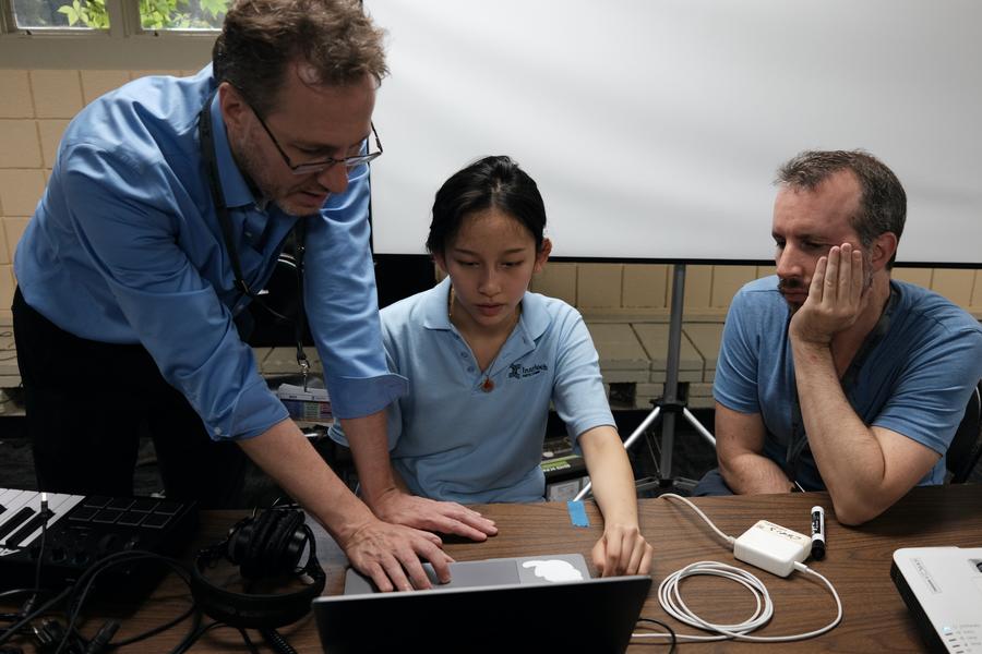 Two faculty members assist a music production student with a laptop.
