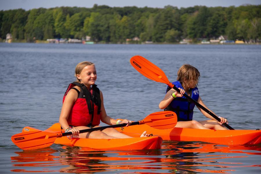 Two happy students paddle canoes across Green Lake.