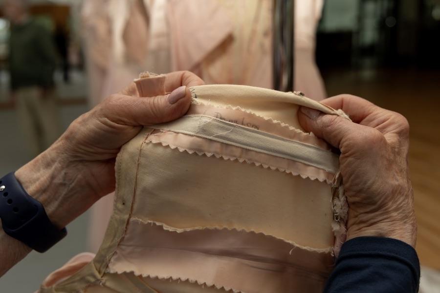An elderly woman's hands are shown pointing out her name inside an old costume.