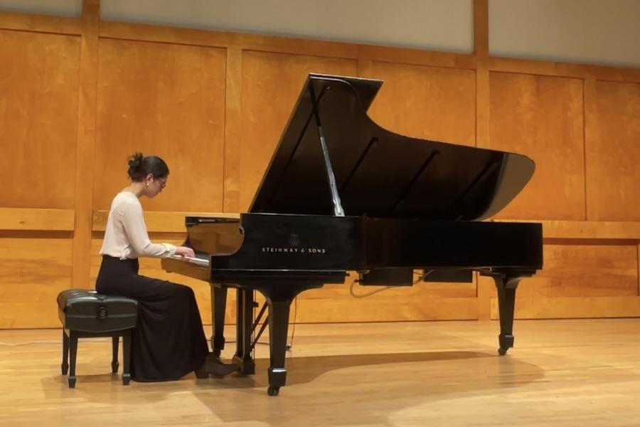 A dark-haired piano student dressed in a long skirt performs at a recital.