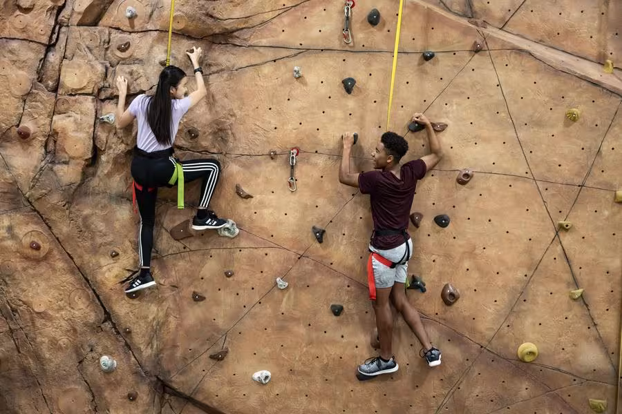 Two students climb a rock wall.