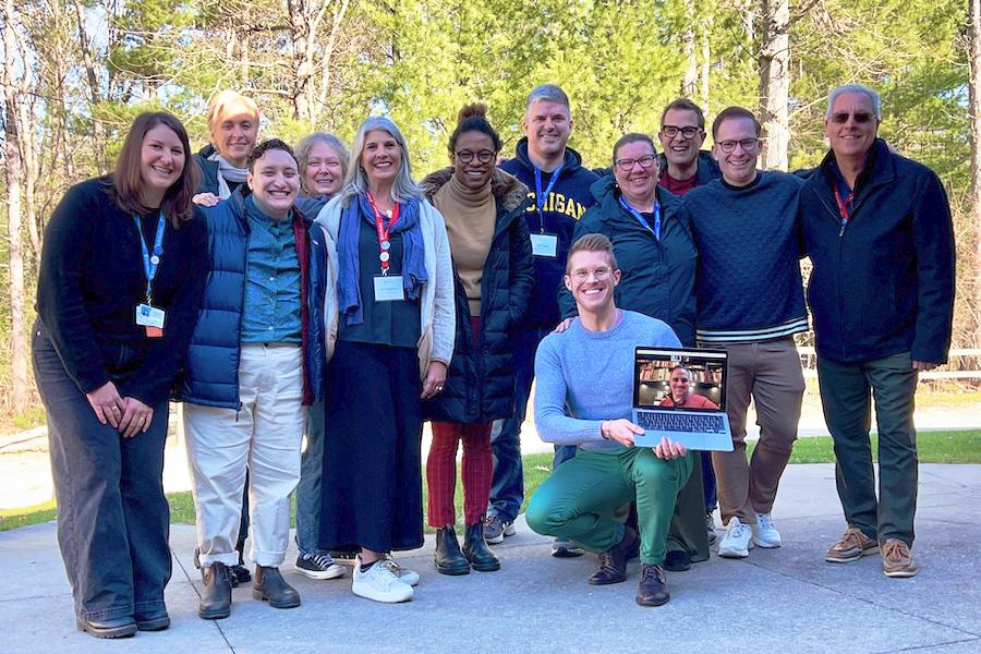 Ten Interlochen Engagement Council members gather with two staff members for group photo on an outdoor patio next to the woods. 