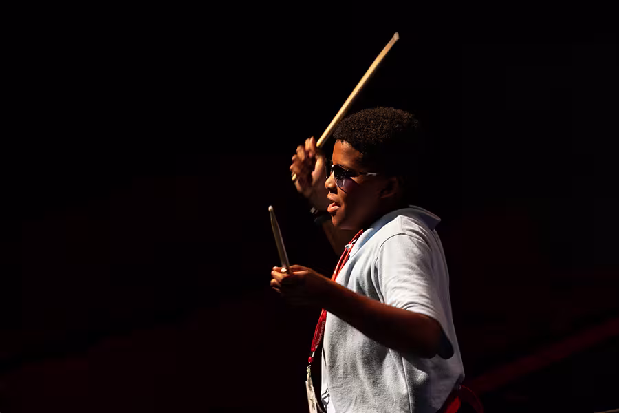 a jazz student wearing sunglasses with drumsticks in the air