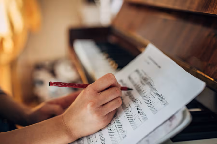Someone writing on sheet music at a piano