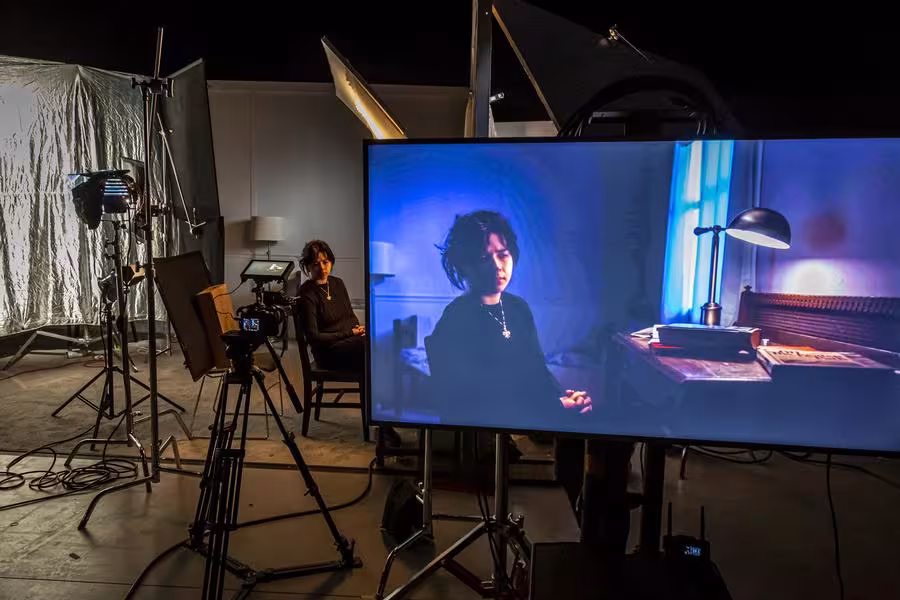 A subject is shown sitting in front of the camera and also within a large viewfinder.