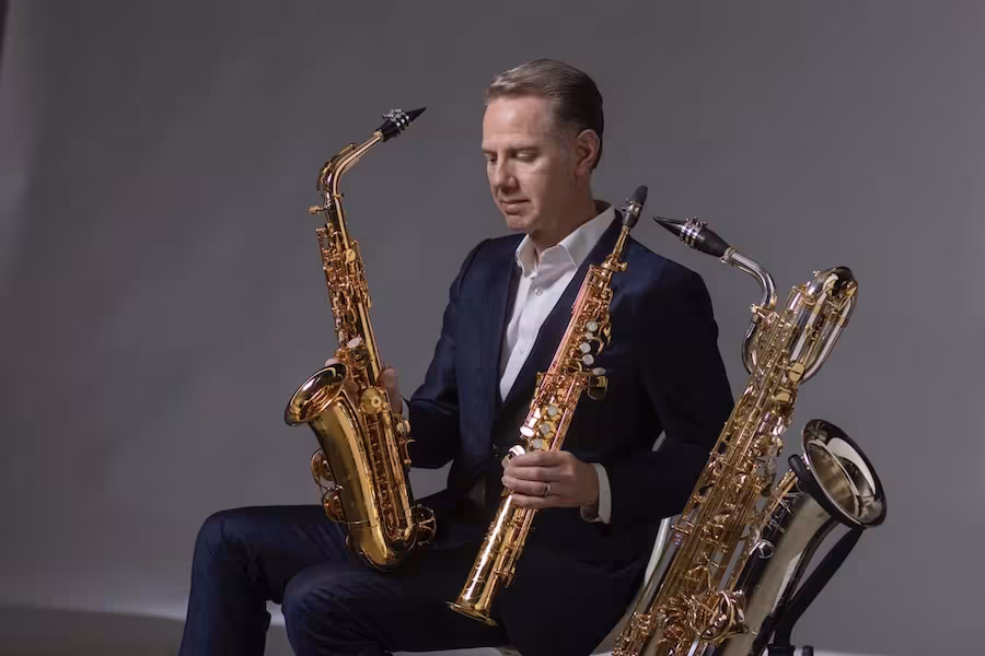 Tim McAllister poses in formal dresswear with three different saxophones.