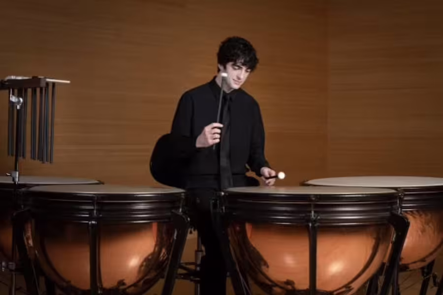 Dressed in a dark suit, a student performs on the drums