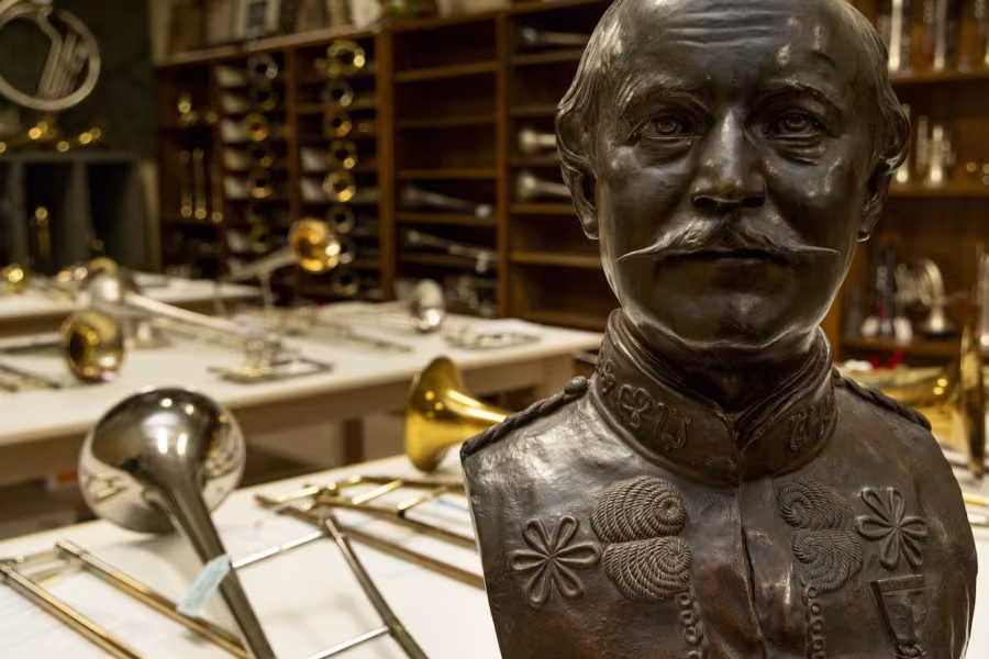 Bronze bust in a room with various brass and woodwind instruments on tables and shelves.