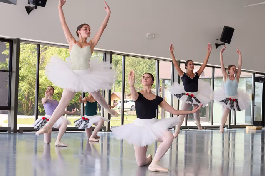Four young dancers in tutus leap into the air, arms outstretched.