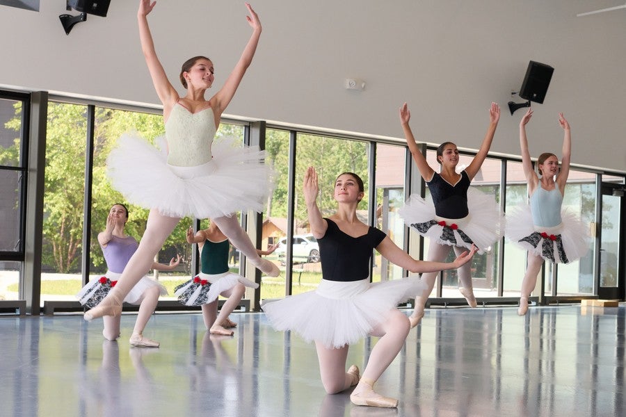 Four young dancers in tutus leap into the air, arms outstretched.