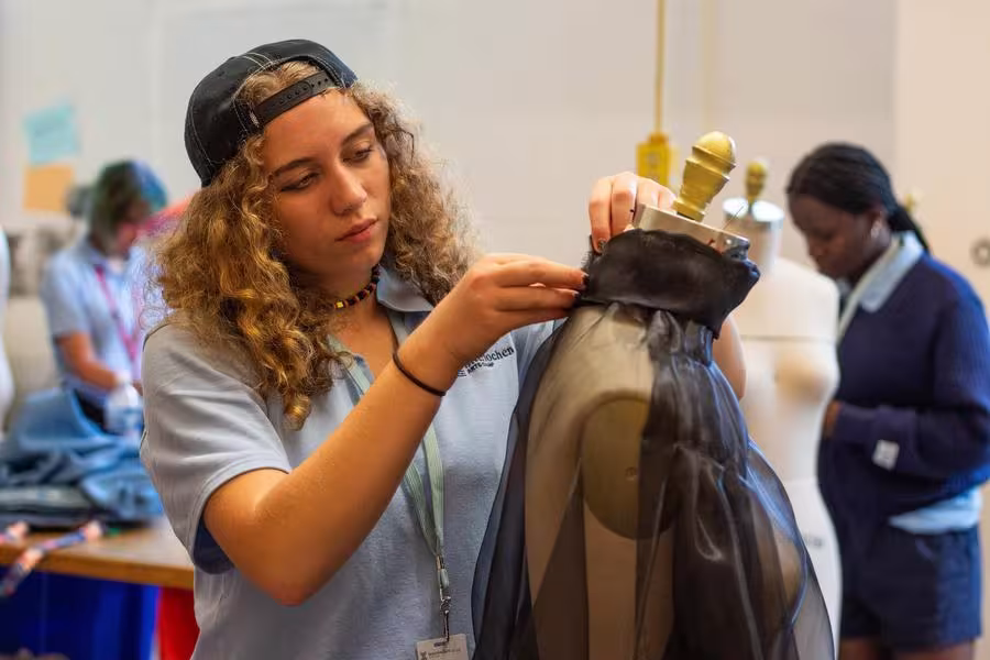 A high school fashion student pins fabric into place on a mannequin.