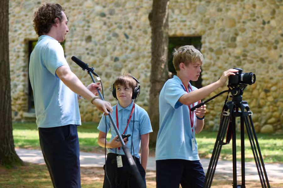 Two students and a counselor set up a shot with a camera and mic.