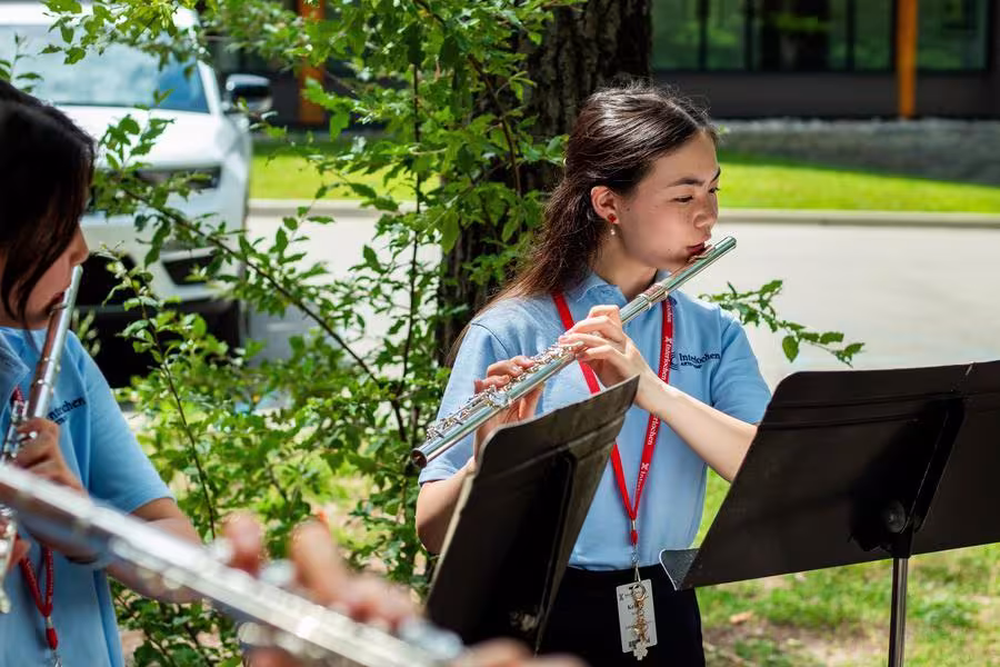 Two students play flutes outdoors.