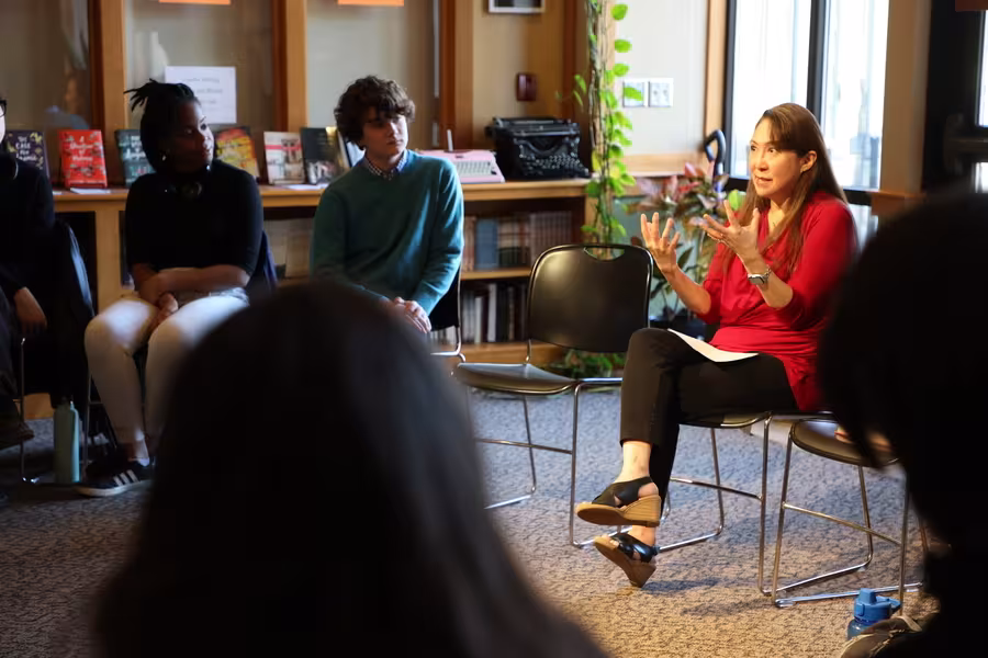 An author dressed in a red blouse sits in a chair and gestures with her hands.