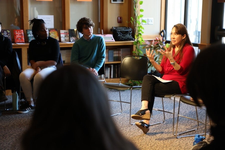 An author dressed in a red blouse sits in a chair and gestures with her hands.
