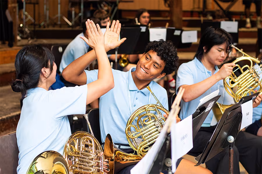 Two World Youth Symphony Orchestra horn players share a high-five during rehearsal.
