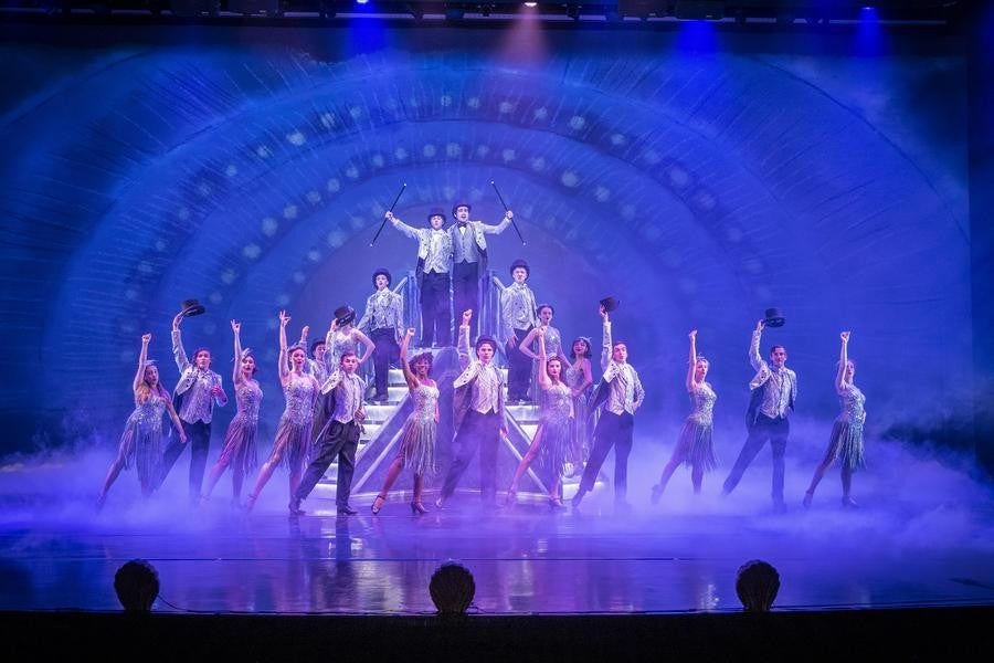 A row of jubilant actors dressed in period attire pose at the end of a dance number.