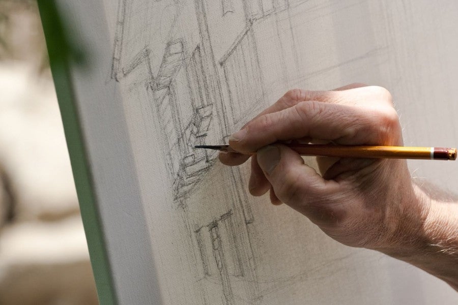 A hand drawing a building with a pencil
