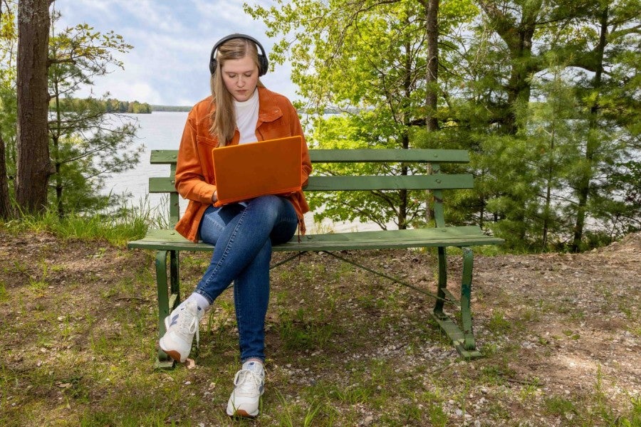 A girl sitting on a bench outside with her laptop