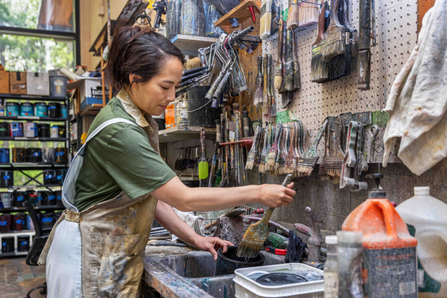 A woman cleaning paint brushes in a workshop